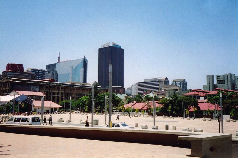 A paved public square in Newtown, Johannesburg, with low buildings, street lights and the city skyline behind.